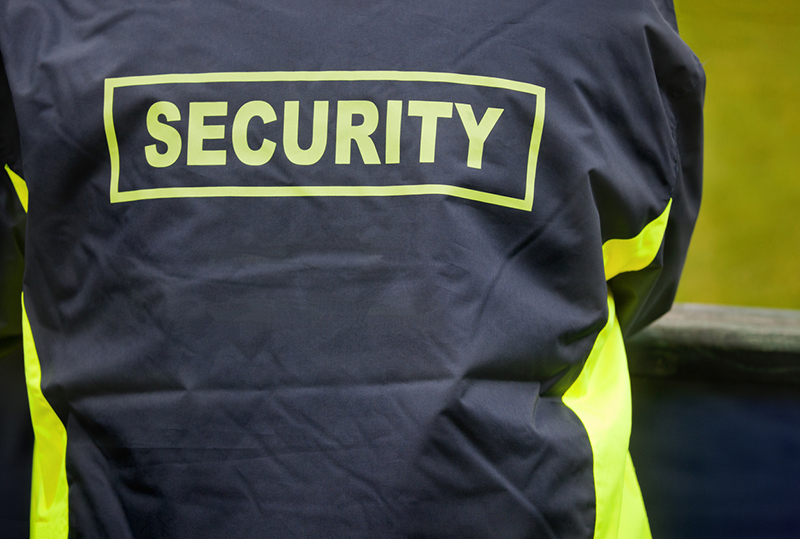 Security staff on duty with high visibility text and jacket panels, stewarding at an outdoor event.