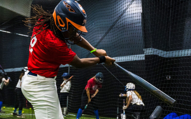 Boy swings baseball bat in indoor training facility.