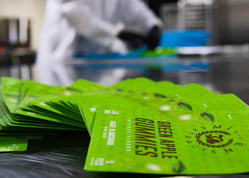 Photo of cannabis edible packaging with lab worker in the background.